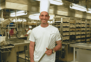 Spring table setting, green plants, purple lace runner, burgundy candle, wine glasses, menu at place setting.